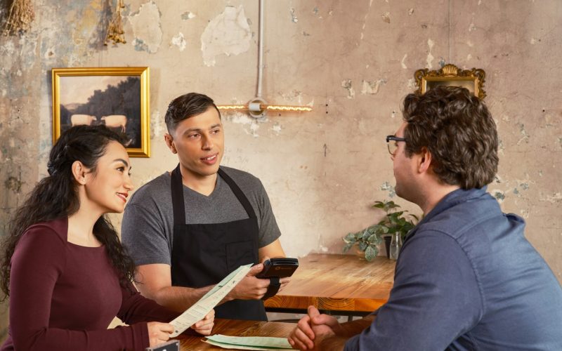 Konobar s POS uređajem poslužuje goste u restoranu